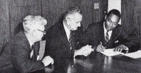 Black and white photo of three men signing paper